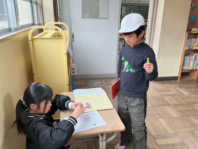 低学年ﾌﾞｯｸｺｰﾅｰで本を借りた子にスタンプを押している様子